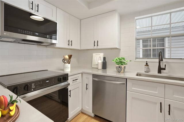 kitchen with sink, light hardwood / wood-style flooring, backsplash, white cabinets, and appliances with stainless steel finishes