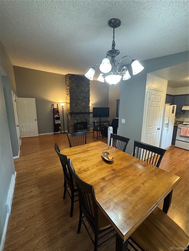 7020 W Portland Ave, Littleton, CO 80128 - dining area with a textured ceiling, a stone fireplace, wood finished floors, and a chandelier