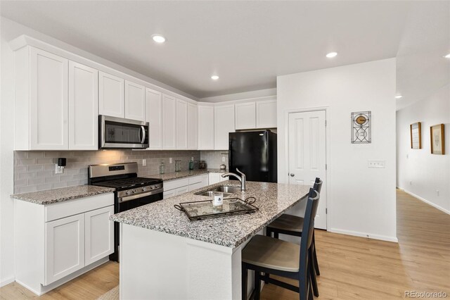 kitchen with light hardwood / wood-style floors, a center island with sink, sink, light stone countertops, and appliances with stainless steel finishes