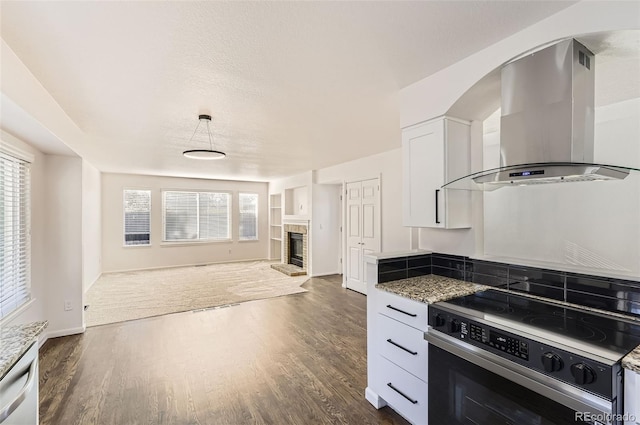 kitchen with electric stove, stone counters, white cabinets, and wall chimney range hood