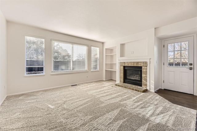 unfurnished living room featuring dark colored carpet, built in features, and a brick fireplace