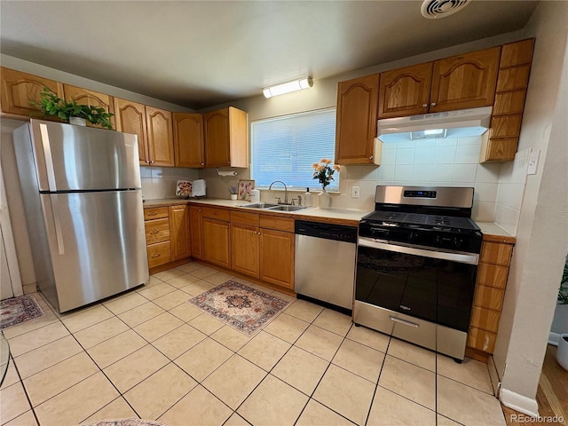 kitchen with tasteful backsplash, stainless steel appliances, light countertops, under cabinet range hood, and a sink