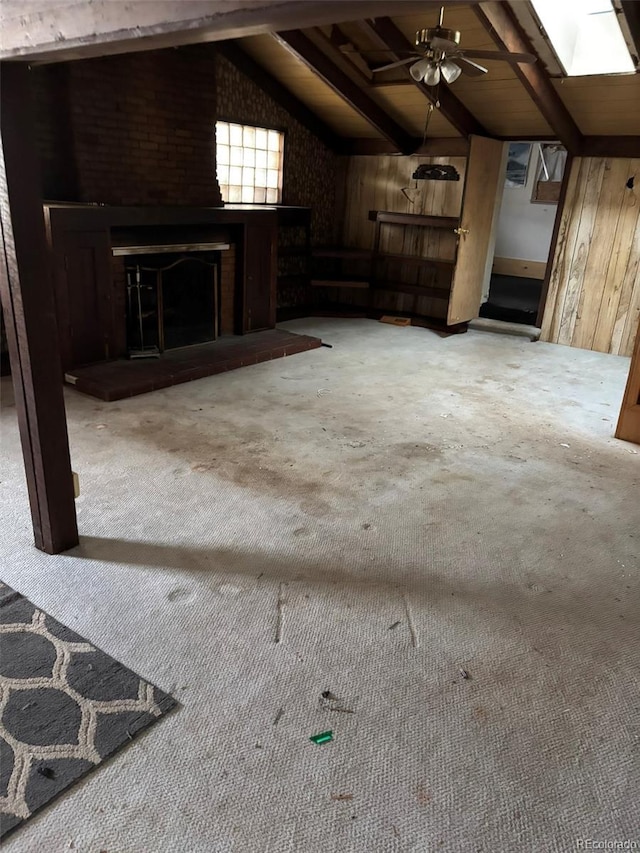 unfurnished living room with carpet flooring, lofted ceiling with skylight, a brick fireplace, and wood walls