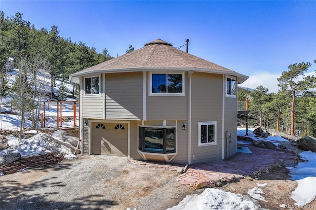 view of front of house with dirt driveway, roof with shingles, and an attached garage