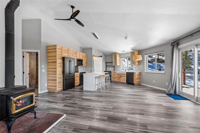 kitchen with a breakfast bar, a center island, a wood stove, black appliances, and a sink