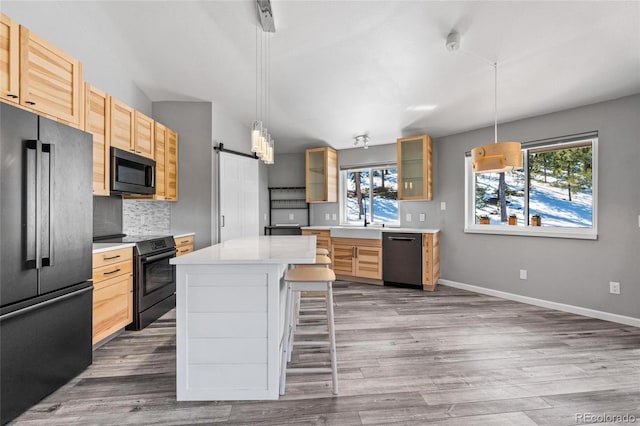 kitchen featuring tasteful backsplash, a barn door, glass insert cabinets, light countertops, and black appliances