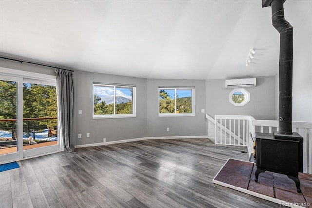 unfurnished living room featuring a wood stove, a wall unit AC, baseboards, and wood finished floors