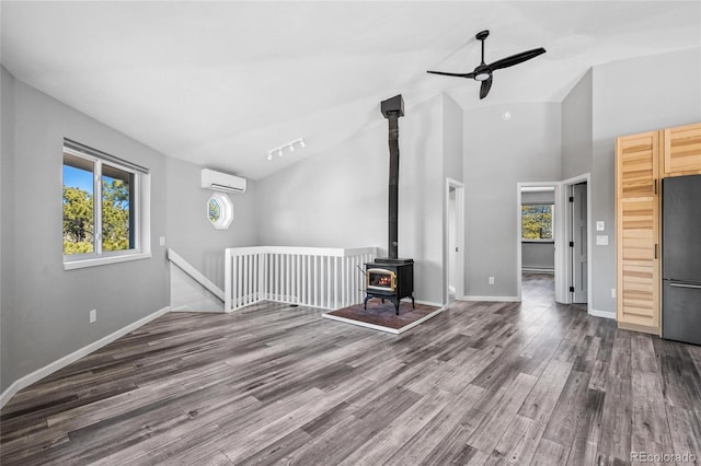 unfurnished living room featuring a wall unit AC, wood finished floors, a wood stove, and baseboards