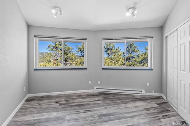 unfurnished bedroom with a closet, a baseboard heating unit, and wood finished floors