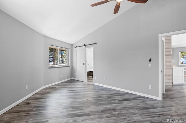 unfurnished bedroom with lofted ceiling, multiple windows, dark wood finished floors, and a barn door