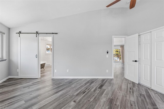 unfurnished bedroom featuring lofted ceiling, wood finished floors, baseboards, and a barn door