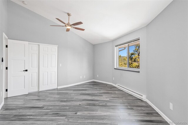 unfurnished bedroom with lofted ceiling, a baseboard heating unit, wood finished floors, baseboards, and a closet