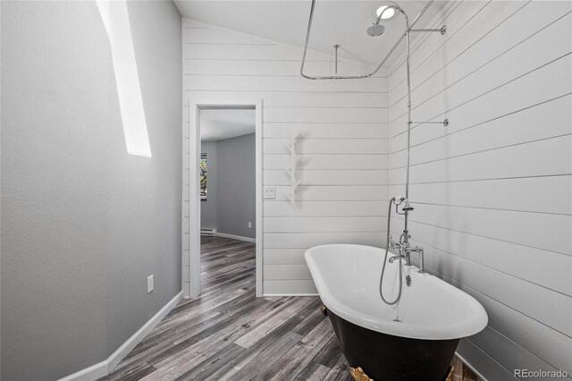 full bathroom featuring wooden walls, baseboards, a soaking tub, wood finished floors, and vaulted ceiling