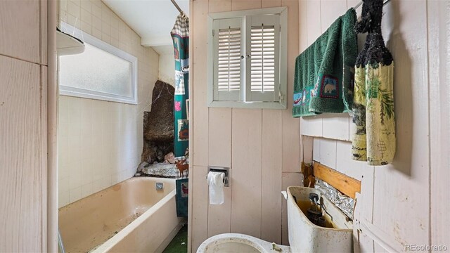 bathroom featuring a bathing tub and wood walls