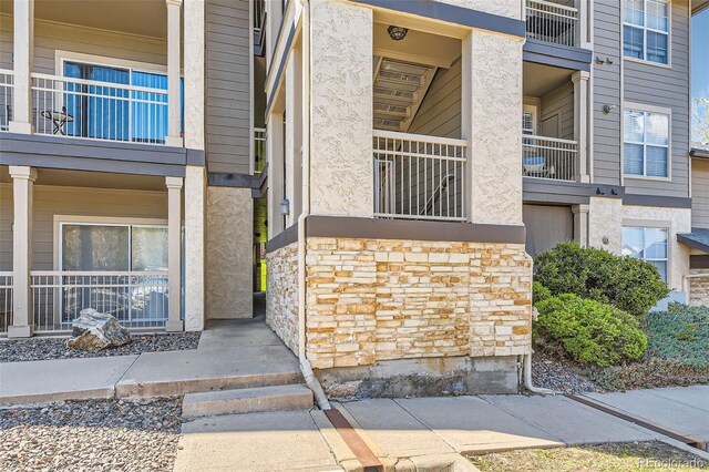 doorway to property featuring stucco siding, stone siding, and a balcony