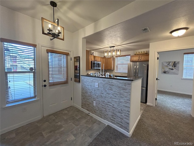 kitchen featuring stainless steel appliances, visible vents, brown cabinetry, dark countertops, and an inviting chandelier