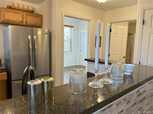 kitchen featuring dark stone counters, freestanding refrigerator, and brown cabinets