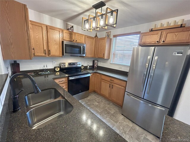 kitchen with brown cabinetry, appliances with stainless steel finishes, dark stone countertops, hanging light fixtures, and a sink