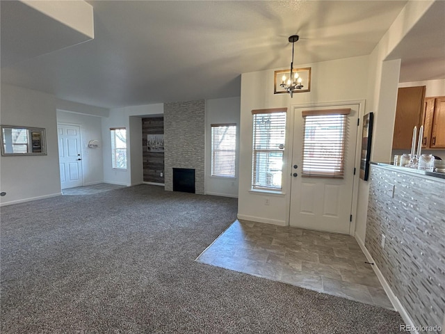 carpeted foyer entrance featuring a large fireplace, stone finish floor, plenty of natural light, and a chandelier