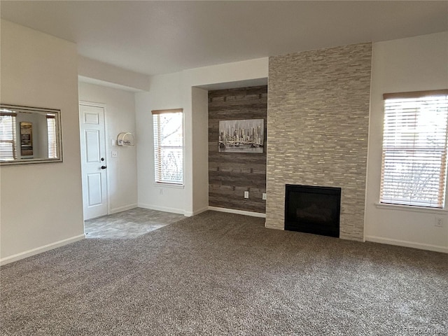 unfurnished living room featuring carpet floors, a fireplace, wood walls, and baseboards