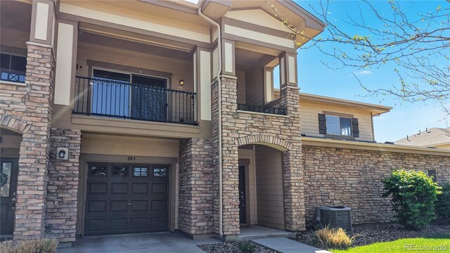 11374 Xavier Dr Unit 202, Westminster, CO 80031 - view of front of property featuring a balcony, central air condition unit, a garage, and stone siding