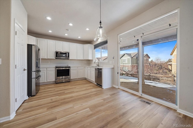 kitchen with appliances with stainless steel finishes, white cabinetry, sink, hanging light fixtures, and light hardwood / wood-style flooring