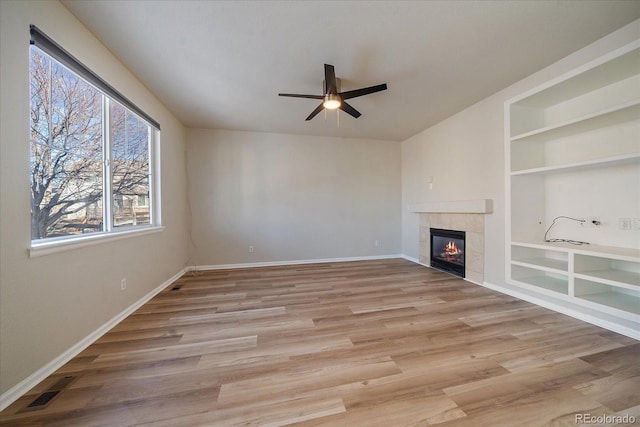 unfurnished living room featuring a fireplace, built in features, ceiling fan, and light hardwood / wood-style flooring