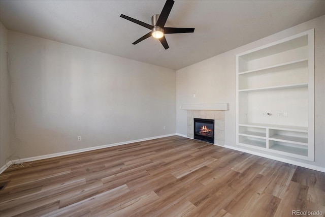 unfurnished living room featuring a tile fireplace, built in features, hardwood / wood-style flooring, and ceiling fan