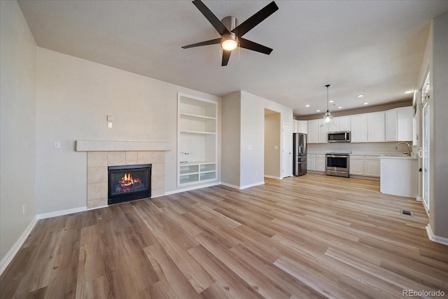 unfurnished living room featuring built in shelves, a fireplace, sink, light wood-type flooring, and ceiling fan