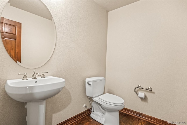 half bath with baseboards, toilet, and wood finished floors