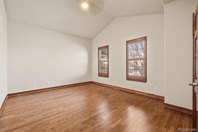 spare room with vaulted ceiling, wood finished floors, visible vents, and baseboards