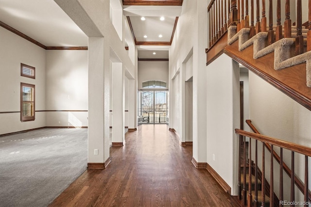 hall with recessed lighting, a towering ceiling, ornamental molding, wood finished floors, and baseboards