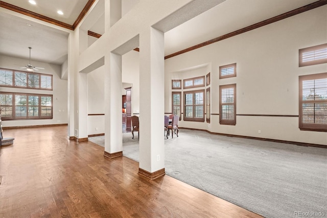 unfurnished living room with crown molding, wood finished floors, a towering ceiling, and baseboards