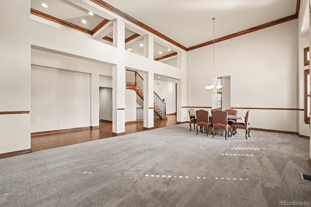 unfurnished dining area with a chandelier, a high ceiling, baseboards, stairs, and crown molding