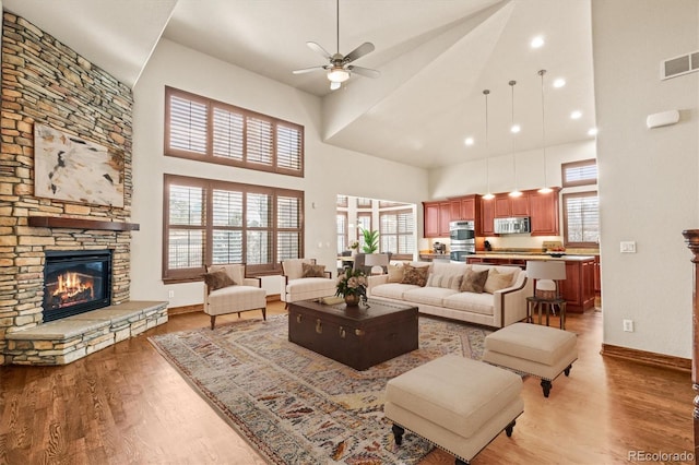 living room featuring a wealth of natural light, baseboards, a stone fireplace, and light wood finished floors