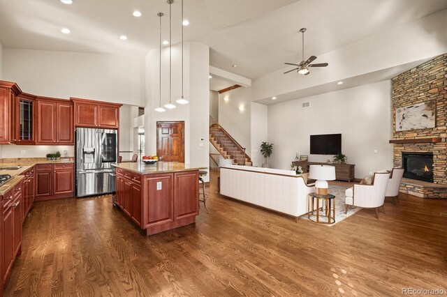 kitchen featuring stainless steel refrigerator with ice dispenser, dark wood-type flooring, glass insert cabinets, open floor plan, and a stone fireplace