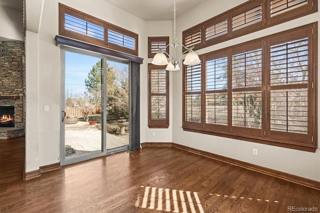 doorway to outside with a notable chandelier, a stone fireplace, baseboards, and wood finished floors