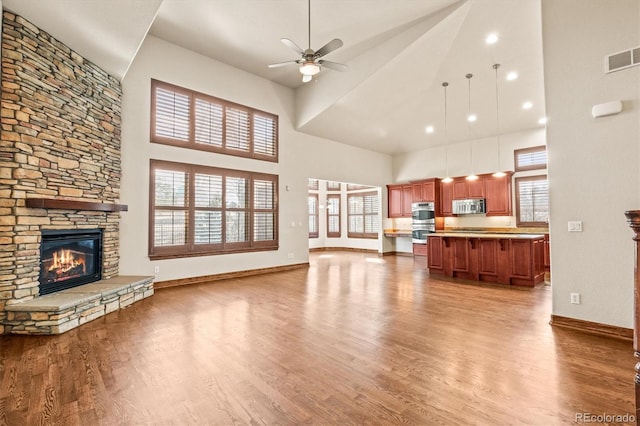 living area featuring a stone fireplace, plenty of natural light, wood finished floors, and a ceiling fan