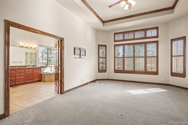 unfurnished room featuring a tray ceiling, crown molding, light tile patterned floors, light carpet, and baseboards