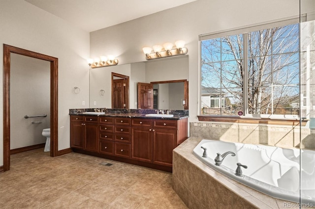 bathroom featuring a garden tub, double vanity, a sink, and toilet