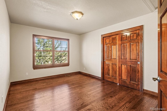 unfurnished bedroom with a textured ceiling, baseboards, and dark wood-type flooring