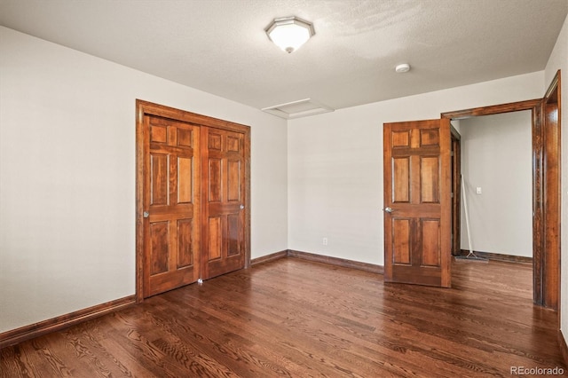 unfurnished bedroom featuring a textured ceiling, dark wood-style flooring, attic access, and baseboards