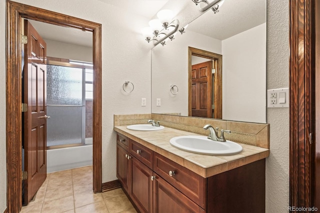 bathroom featuring double vanity, shower / bath combination with glass door, tile patterned flooring, and a sink