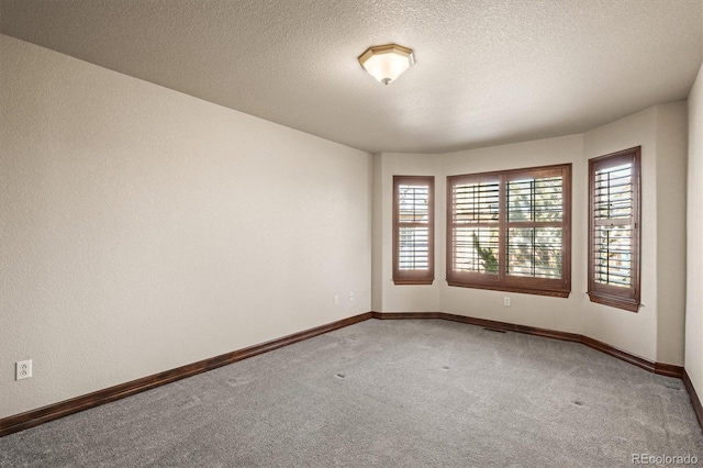 empty room with light carpet, baseboards, and a textured ceiling