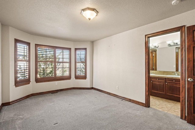 unfurnished room featuring a textured ceiling, baseboards, a sink, and light colored carpet