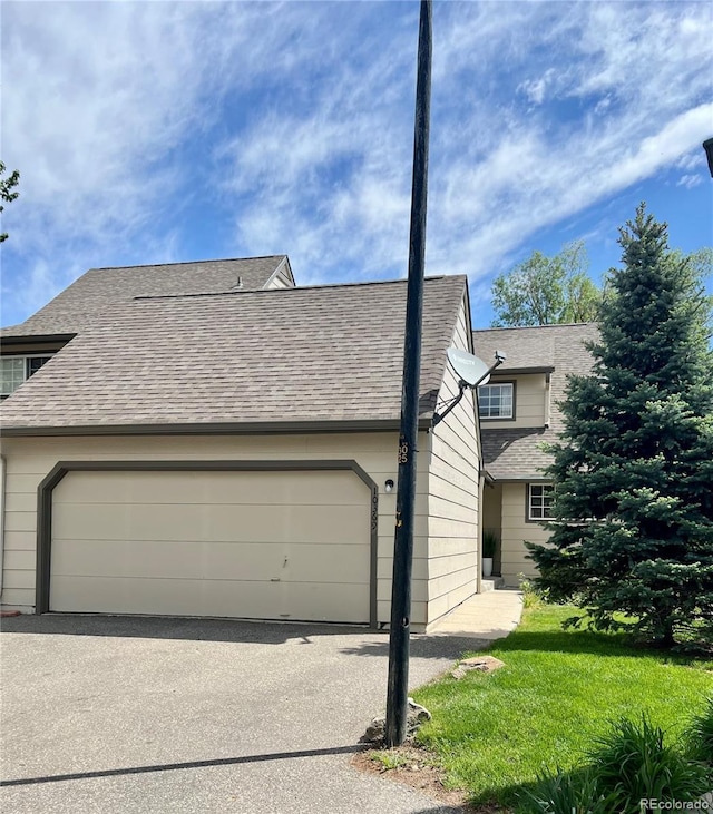 view of side of home with roof with shingles, an attached garage, and asphalt driveway