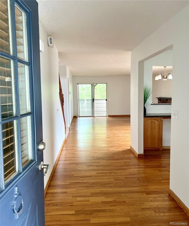 hallway featuring wood finished floors, a textured ceiling, baseboards, and a chandelier