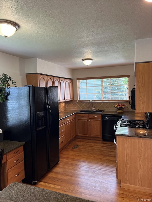 kitchen with black appliances, a sink, light wood-type flooring, decorative backsplash, and a textured ceiling