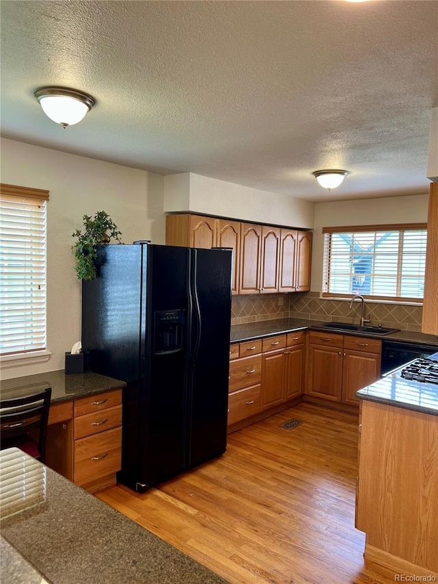 kitchen featuring a sink, black fridge, light wood-style floors, a textured ceiling, and backsplash