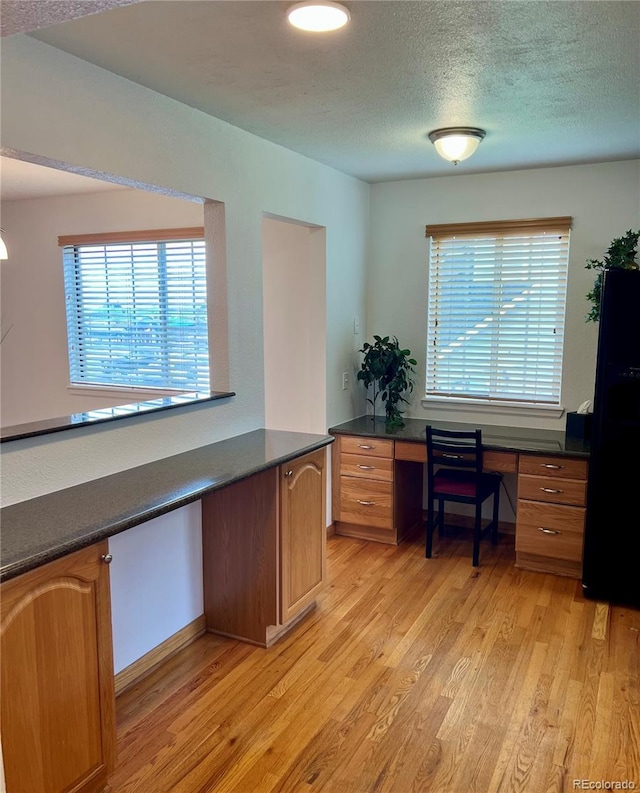 office featuring light wood-type flooring, built in study area, healthy amount of natural light, a textured ceiling, and baseboards
